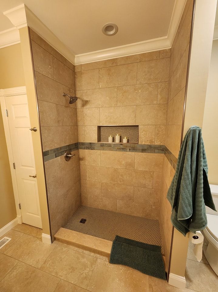 A tiled walk-in shower with a pebble floor, built-in shelf, and two shower heads. A towel hangs on the right.