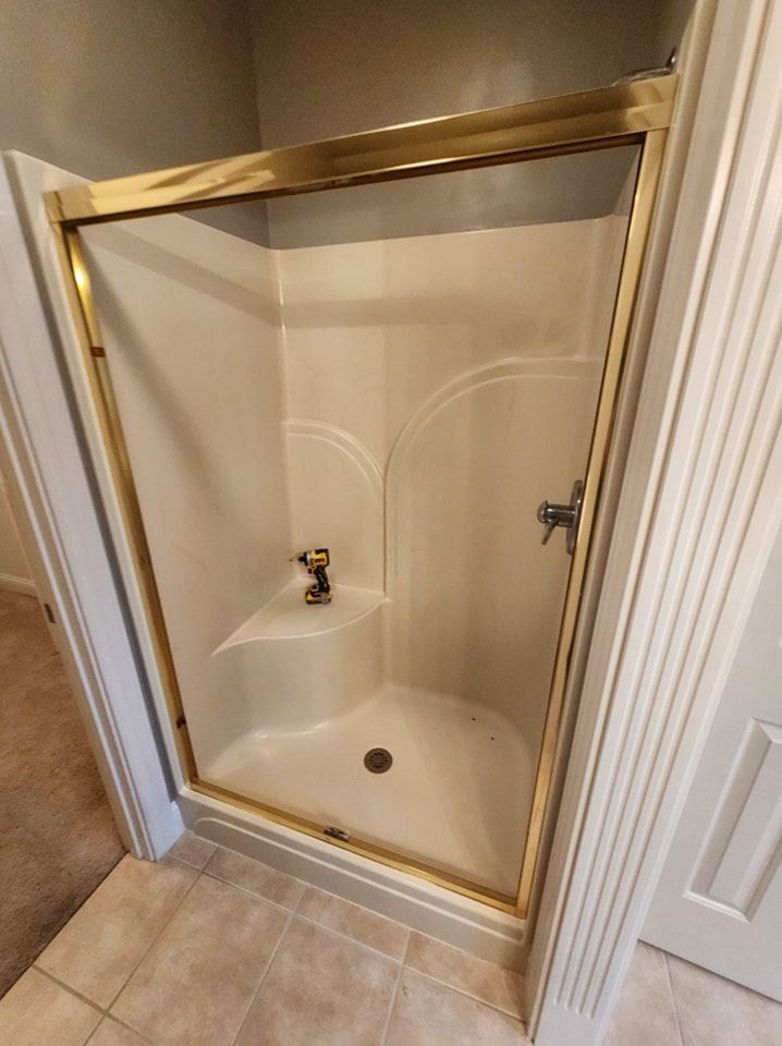 Corner shower stall with gold trim, beige walls, and a small built-in seat.