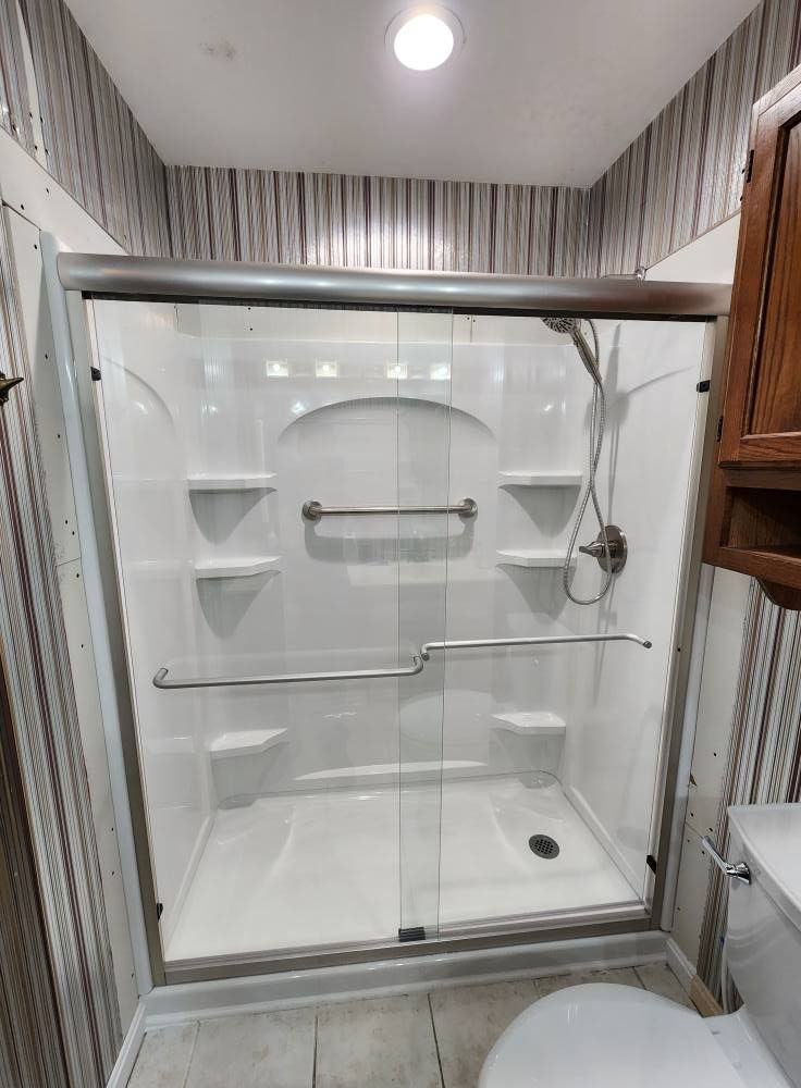 A white shower enclosure with sliding glass doors, grab bar, and built-in shelves.