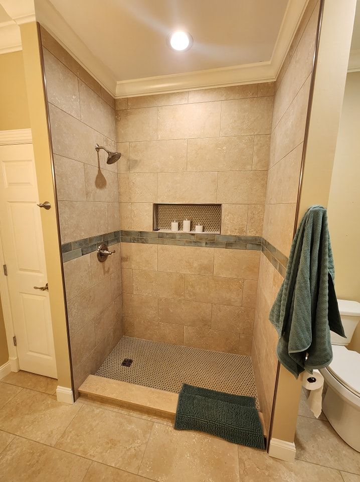Bathroom shower with beige tile, recessed shelf, and green towel.