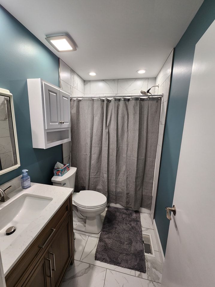 Bathroom with teal walls, a white vanity, a toilet, and a gray shower curtain.