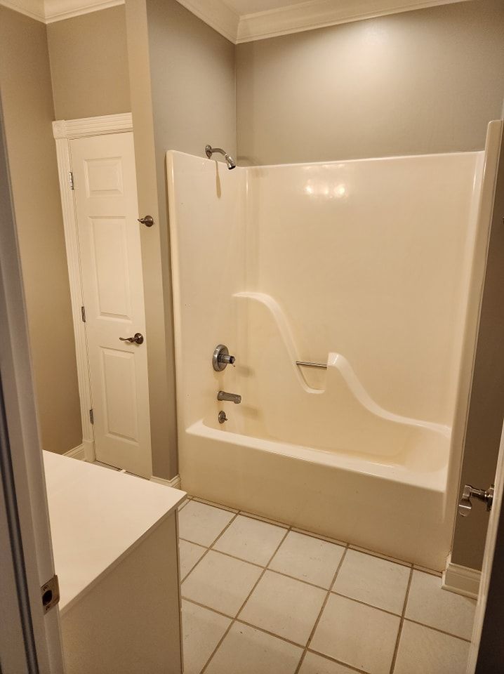 Bathroom with white bathtub/shower combo, tile floor, and a closed white door.