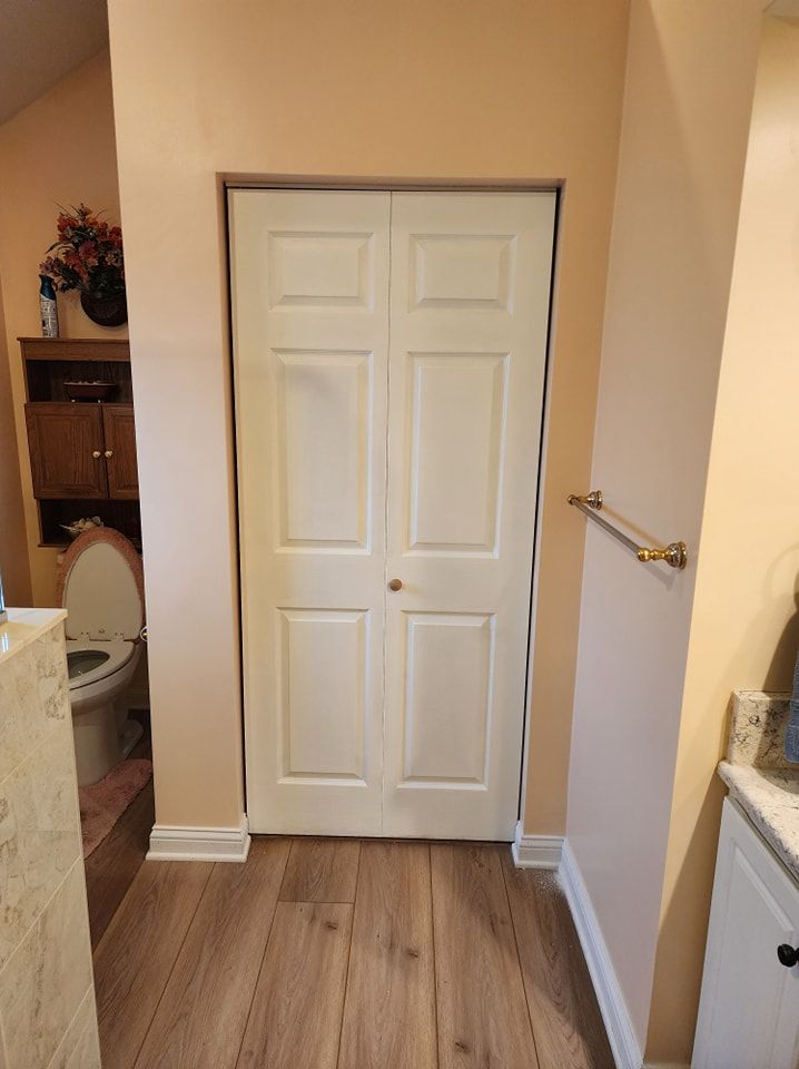 Bathroom with closed white bi-fold door, toilet, and vanity with towel rack, in a room with light peach walls.