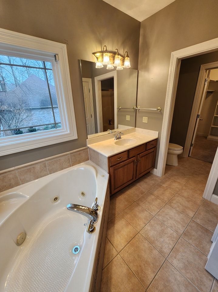 Bathroom with a white jacuzzi tub, vanity, and tan tile floor.