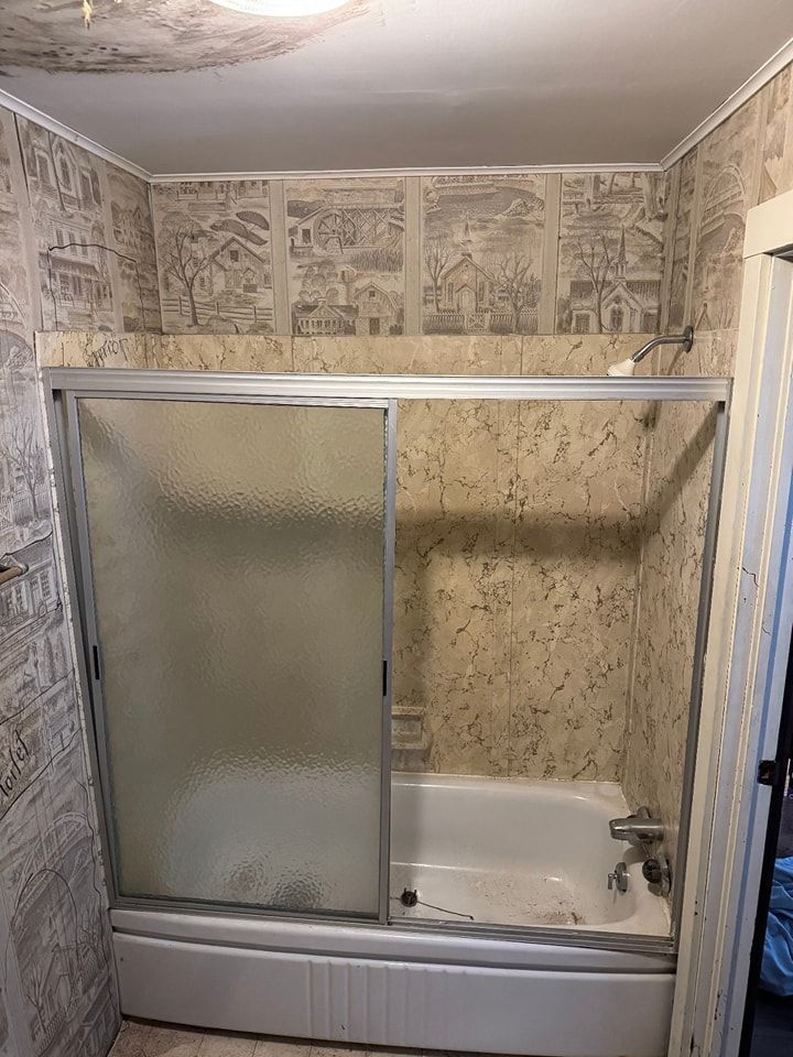 Bathroom with a white tub, sliding glass shower doors, and patterned walls.