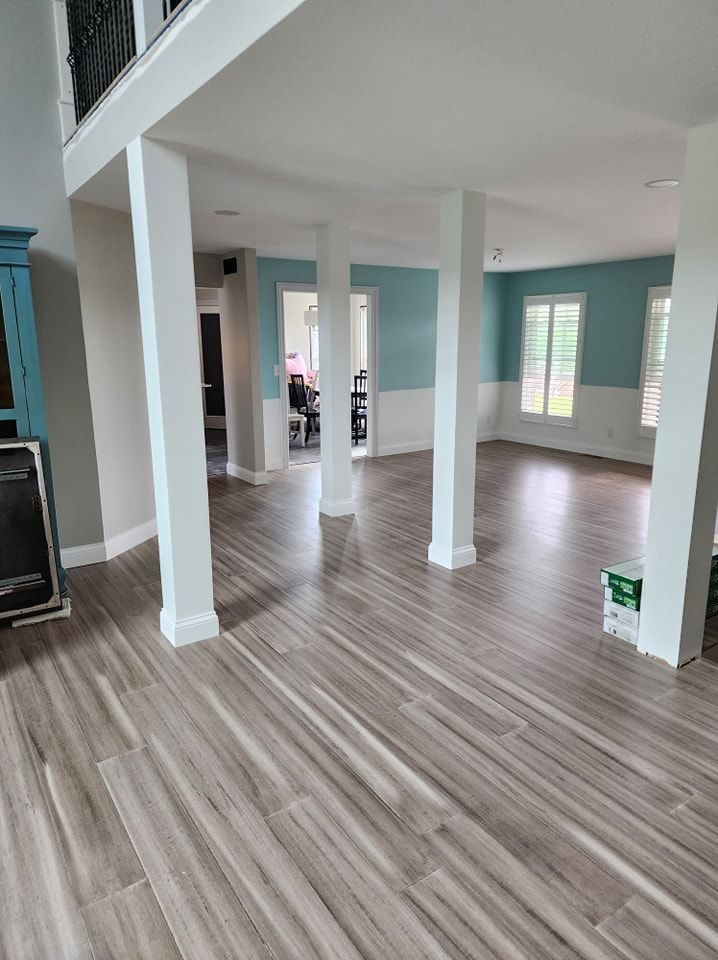 Empty room with wood-look tile flooring, white pillars, light blue walls, and large windows.