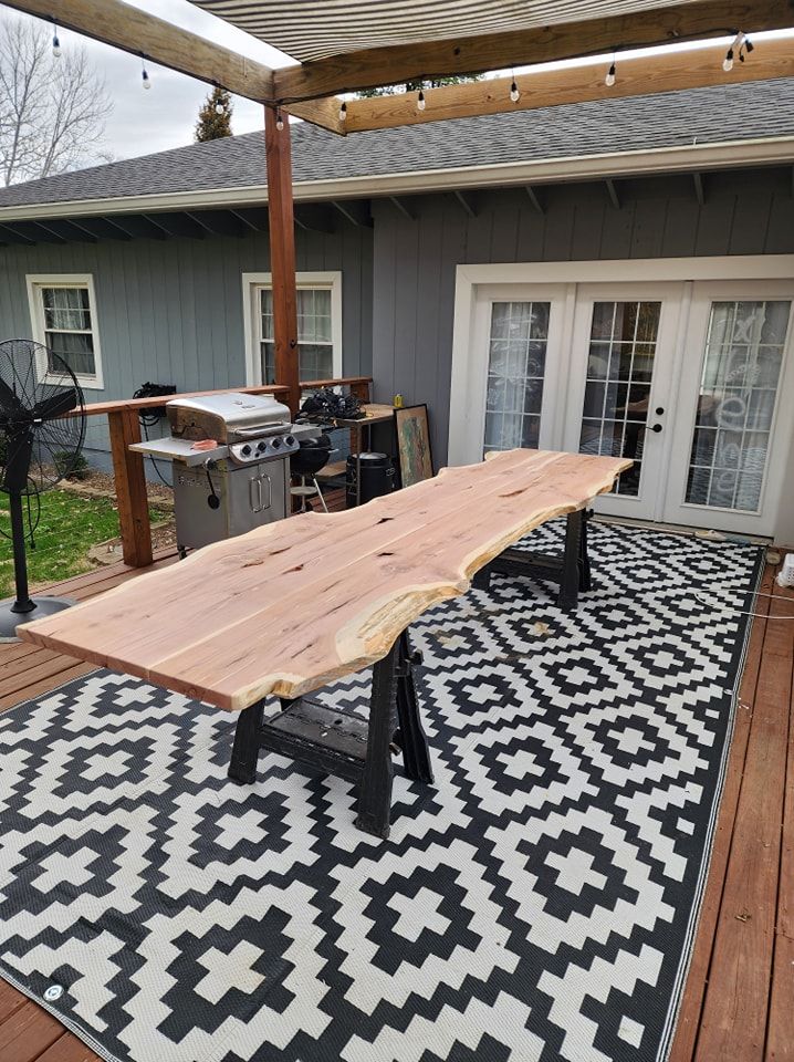 Live edge wooden table on sawhorse legs outdoors on patio rug.