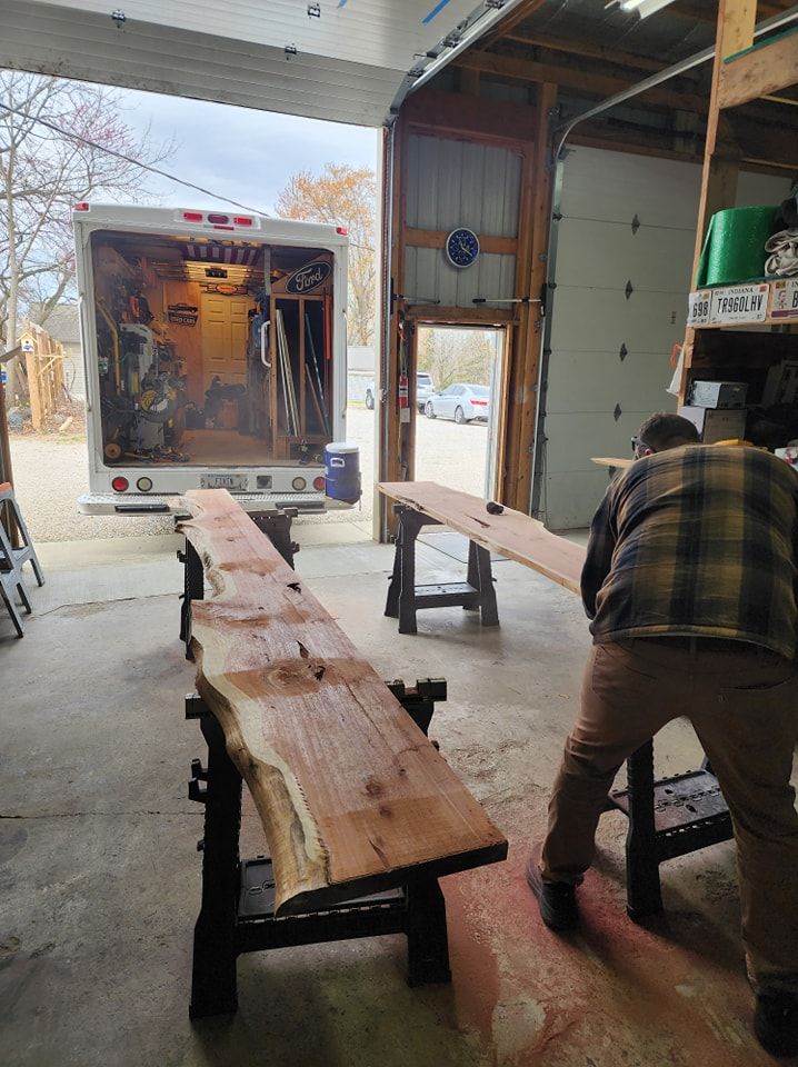 Person working with wood slabs in a workshop, with a truck in the background.
