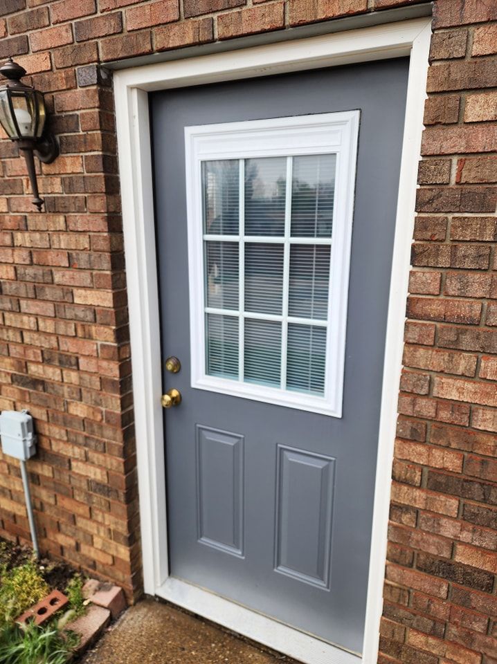 Gray door with white trim set in brick wall; has window panes.