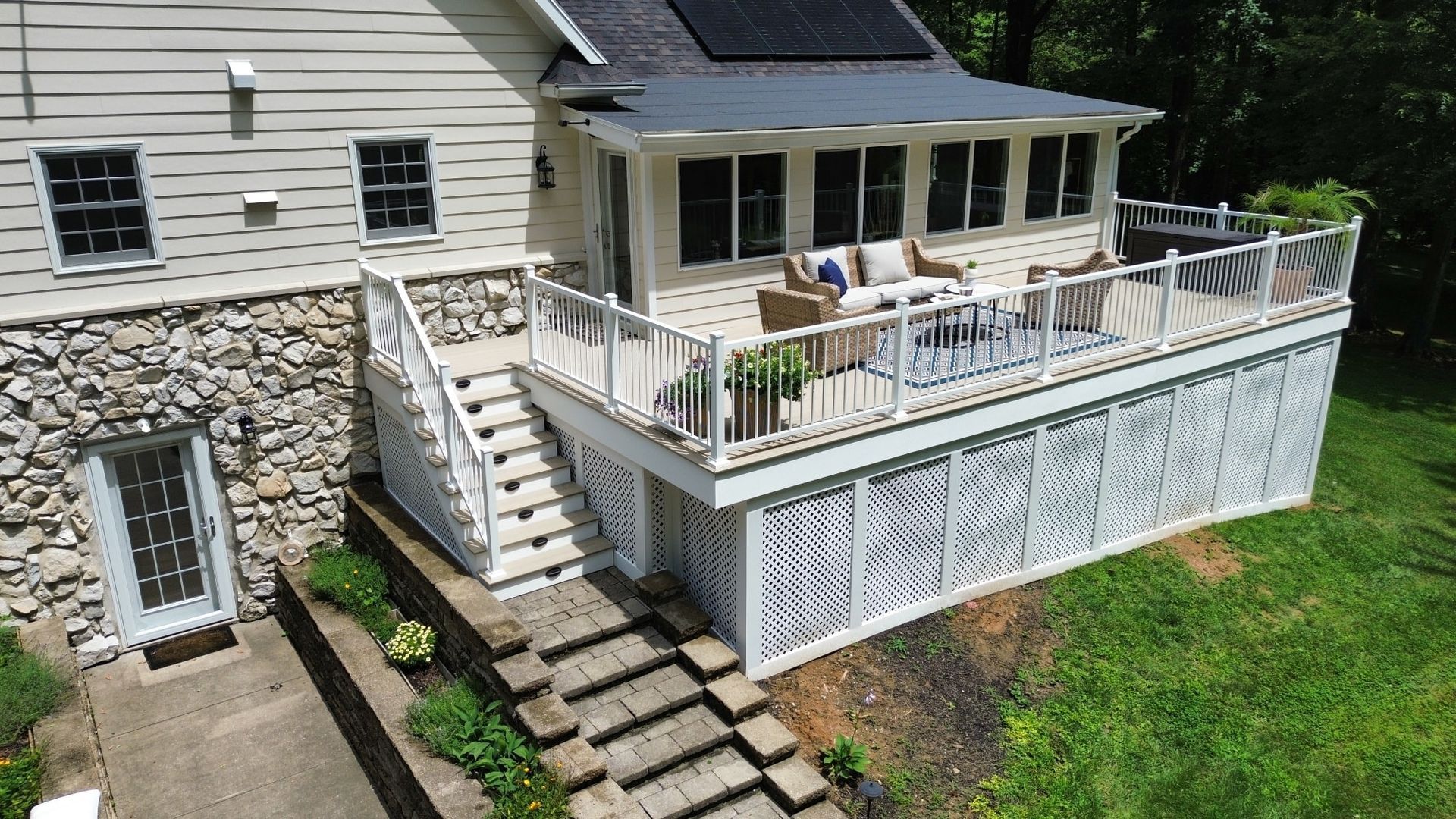 House exterior with a deck, screened porch, and stone foundation. White railings, stairs, and decorative skirting.