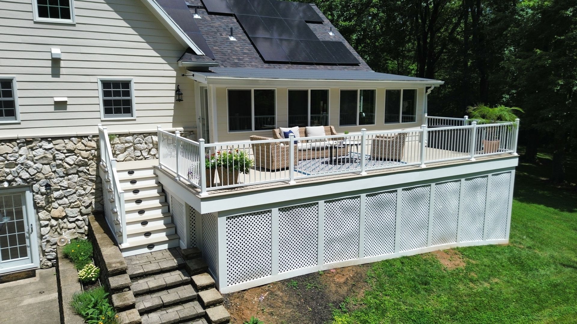 Multi-level white deck with screened-in porch, attached to a light-colored house with stone foundation, overlooking a grassy yard.