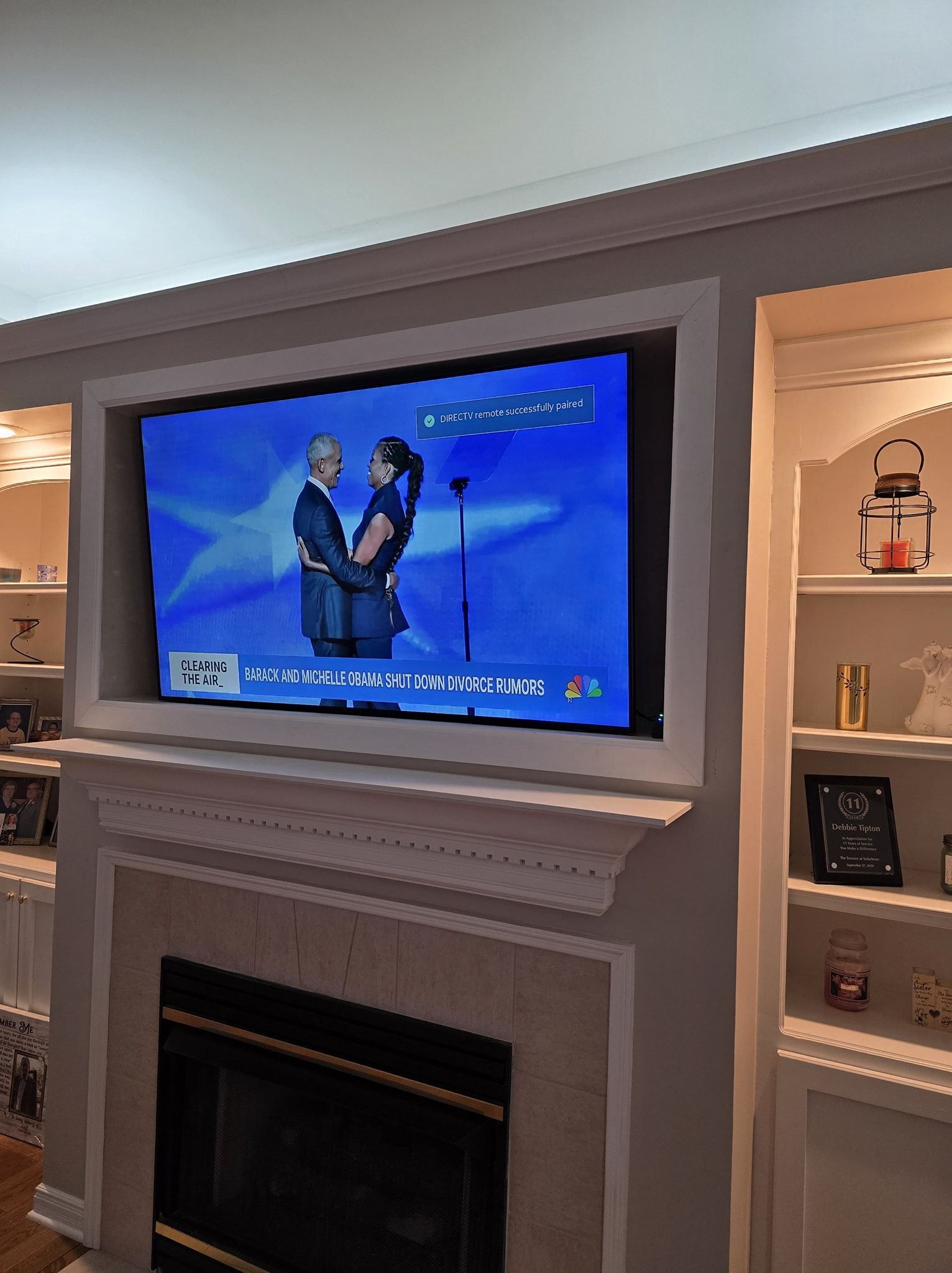 TV displaying news, mounted above a fireplace with built-in bookshelves on one side.