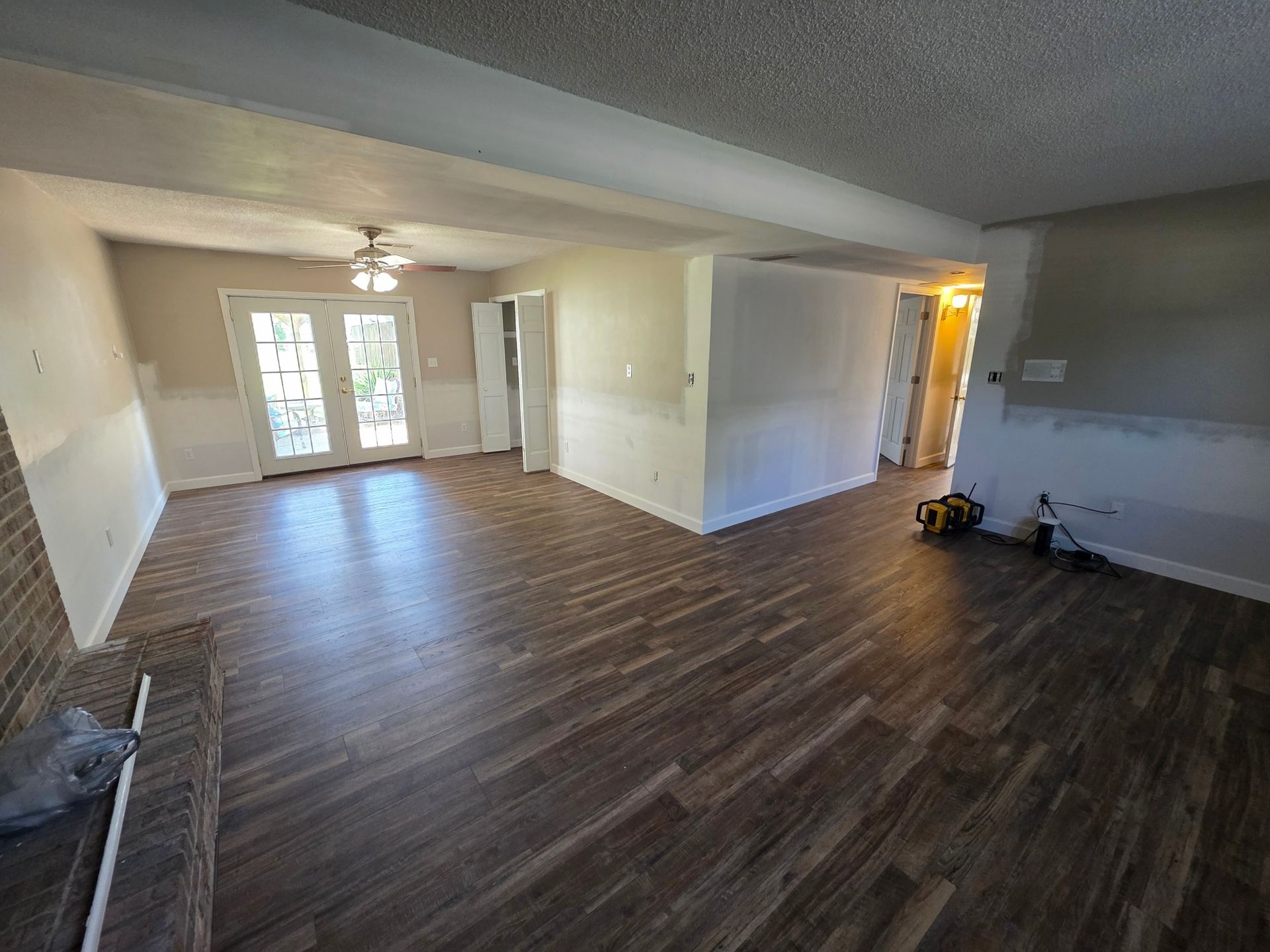 Newly renovated living room with dark wood-look flooring, white walls, and French doors leading outside.