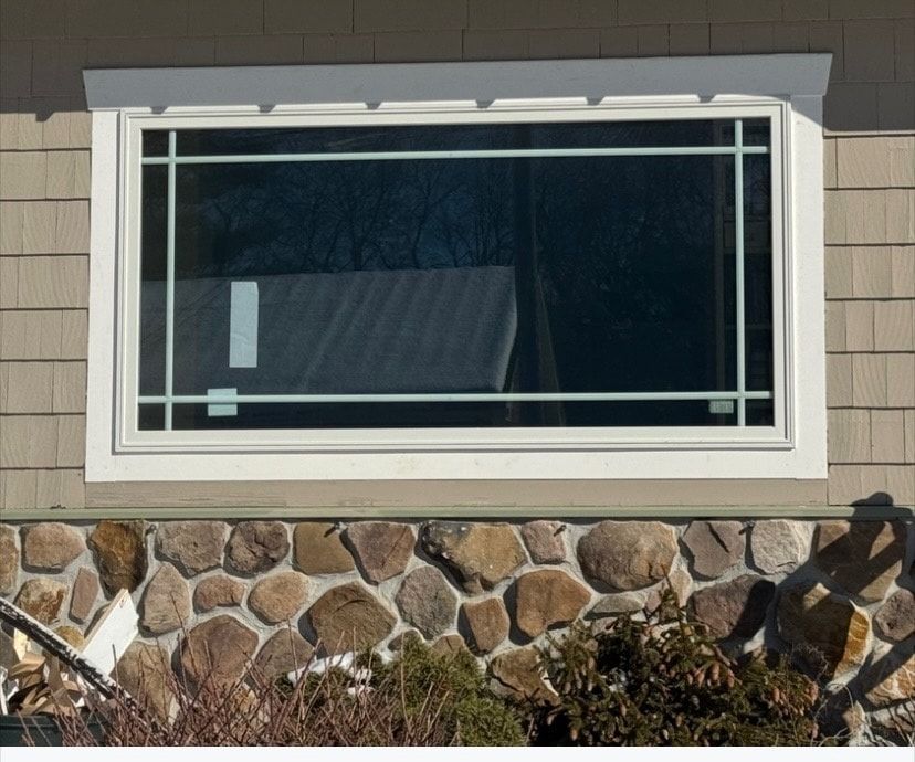 Large rectangular window with white trim, grids, and beige stone foundation.