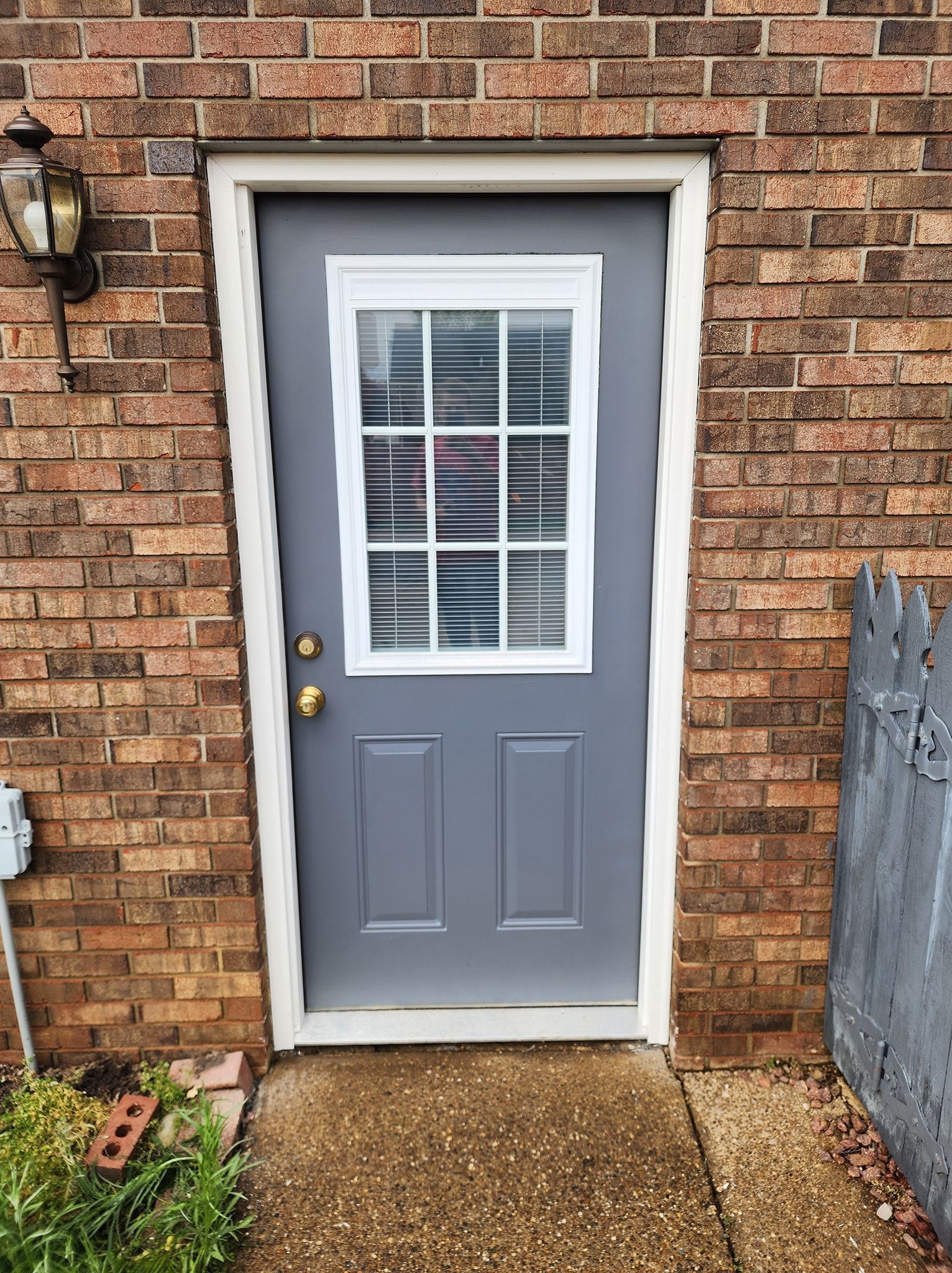 Gray door with window, brick building exterior.