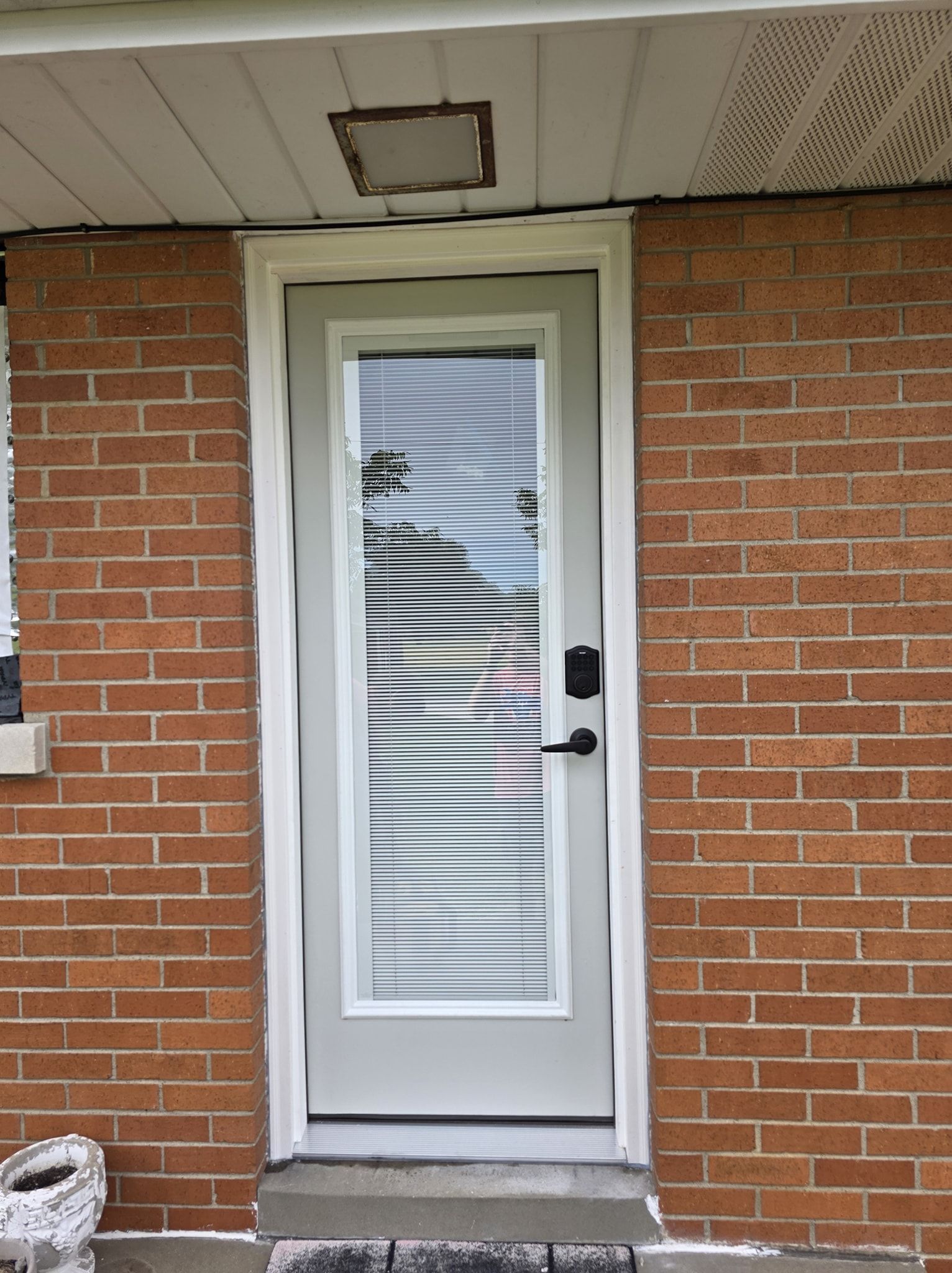 Exterior door with window and blinds in a brick wall. Gray door frame and white trim.
