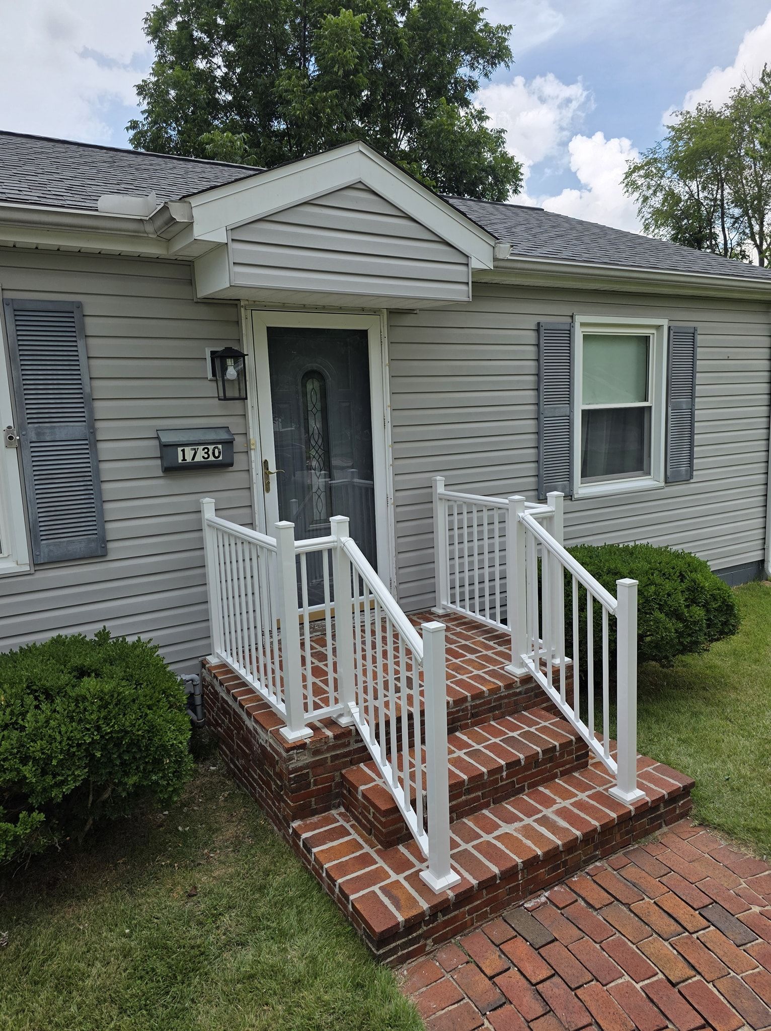 Gray house with red brick steps, white railing, and gray shutters.