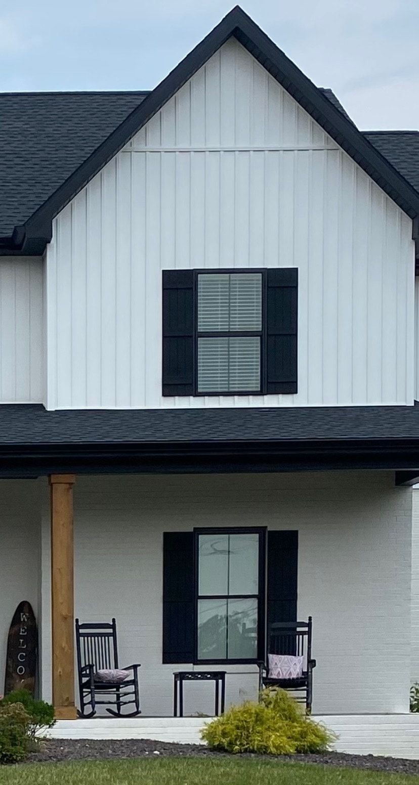 White and black farmhouse with shutters; porch with rocking chairs.
