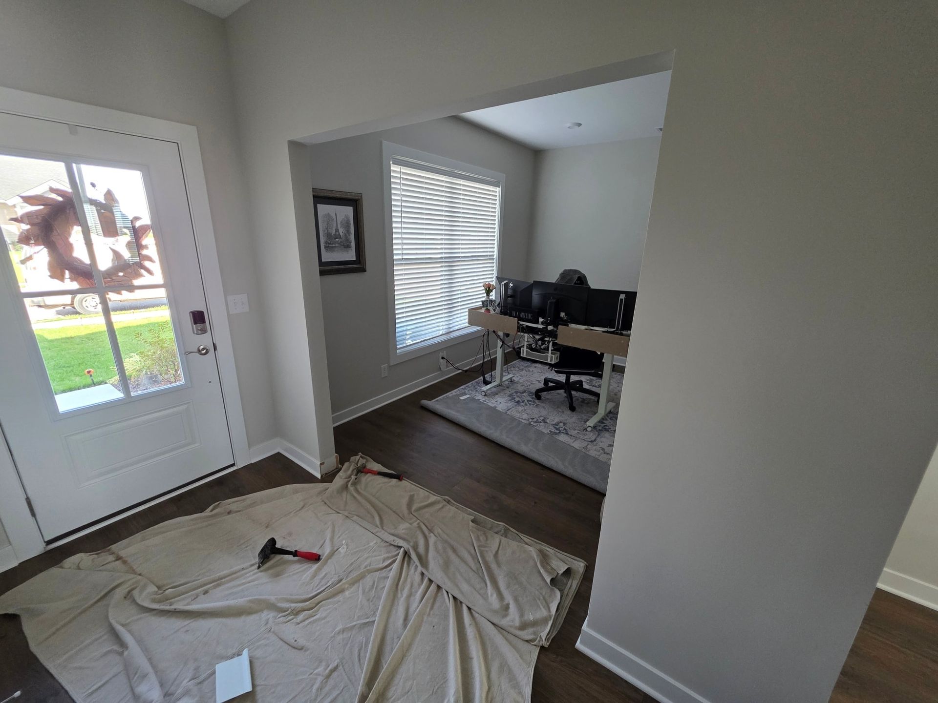 Entryway with open doorway to an office. A large tarp and hammer lie on the floor.