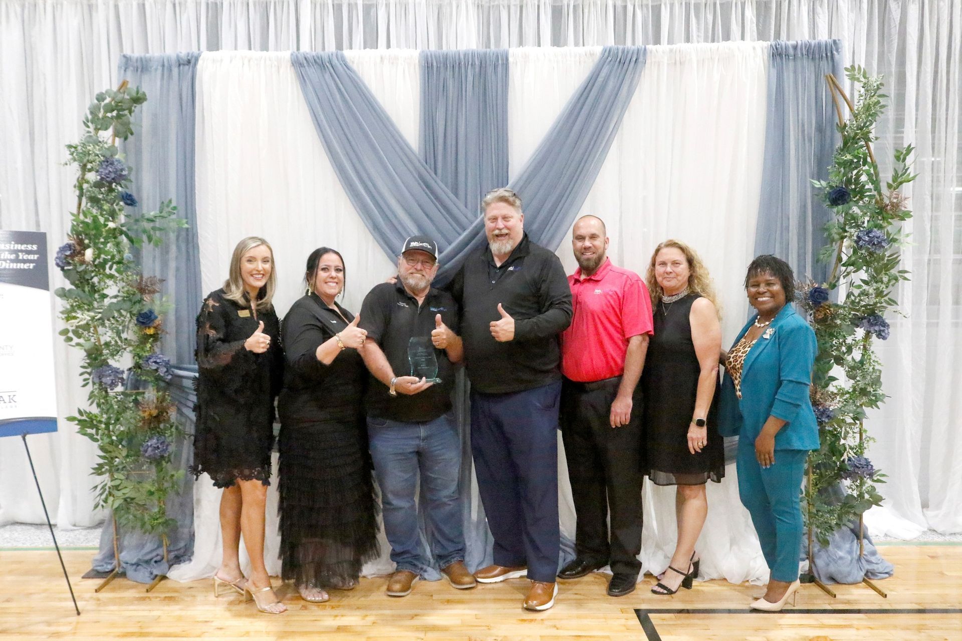 Group of people posing for a photo at an event, standing in front of a backdrop with a sign.