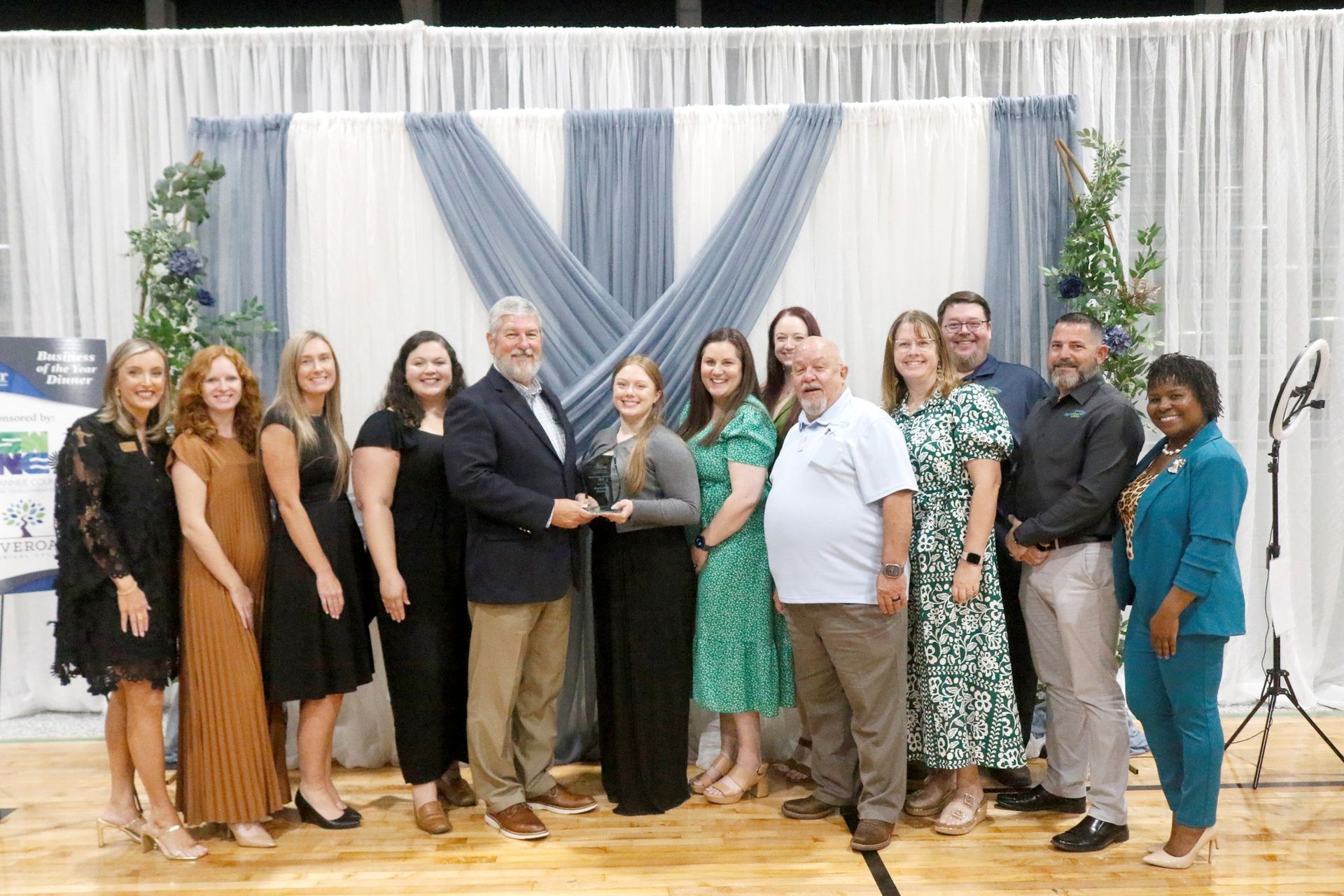 Group of people holding an award, smiling, standing in front of a sparkly backdrop.