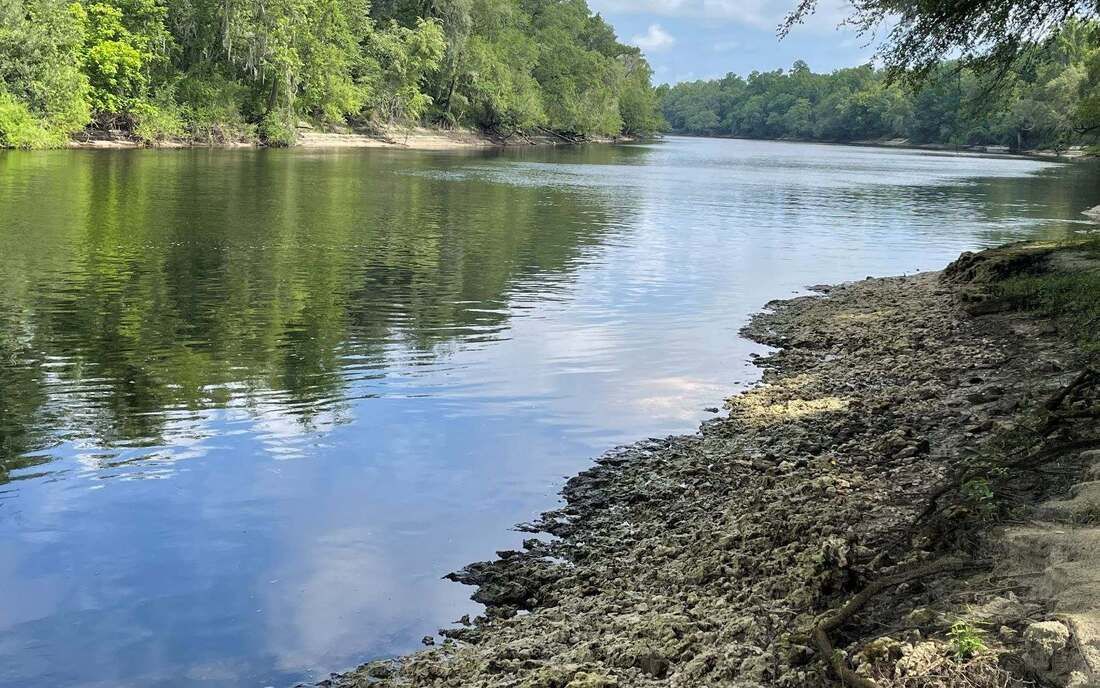 River scene with rocky shoreline and reflections of trees in the water.