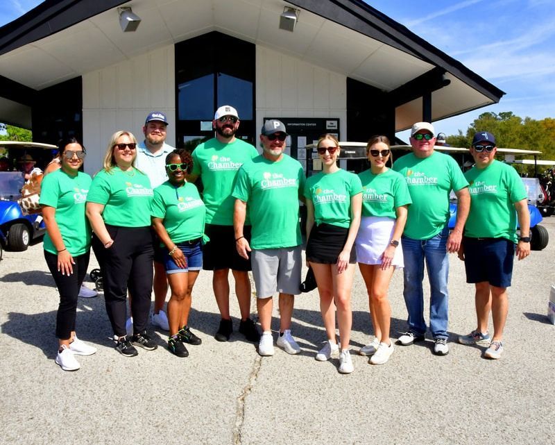 Group of people in green shirts posing in front of a building, likely at a golf course.