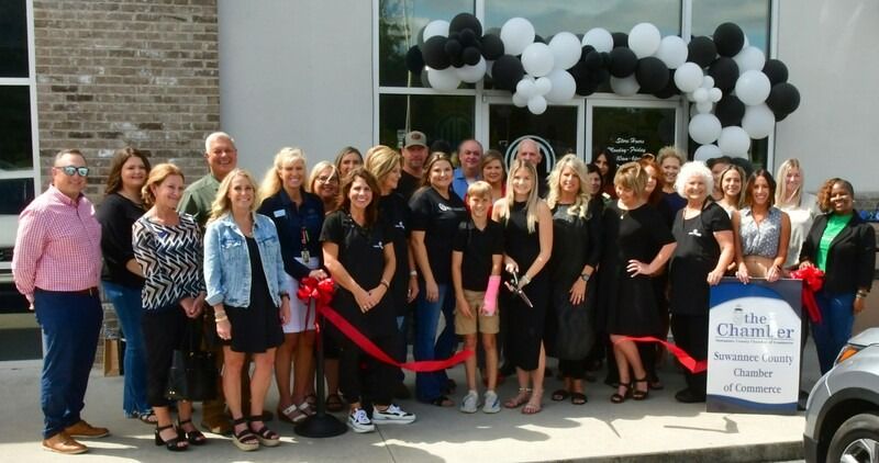 Group of people cutting a ribbon in front of a building with black and white balloons.