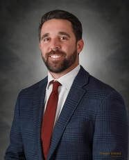 Man in a blue plaid suit and red tie smiles, posing in front of a gray backdrop.