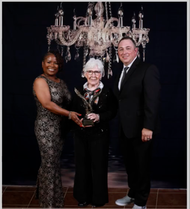 Three people with award, posing in front of chandelier. 