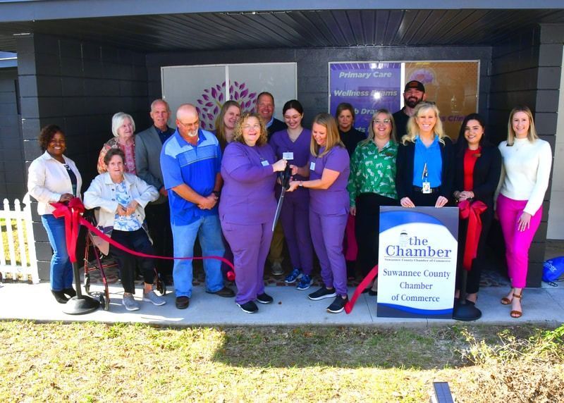 People cutting a ribbon at a chamber of commerce event, building exterior in background, sign for the chamber.