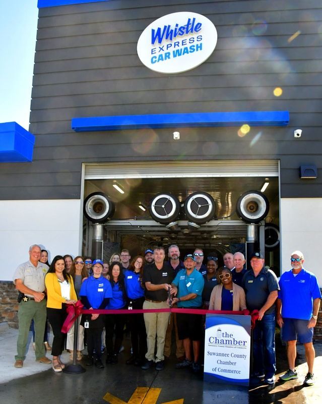 Ribbon-cutting at Whistle Express Car Wash grand opening. Group of people smiles in front of the car wash entrance.