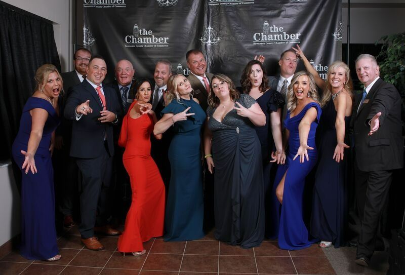 Group of people in formal attire pose for a photo in front of a banner.