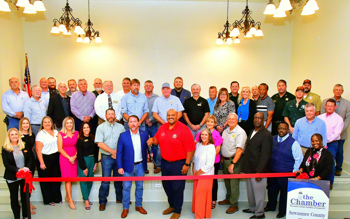 Group of people at a ribbon-cutting ceremony. Red ribbon stretched across the front.