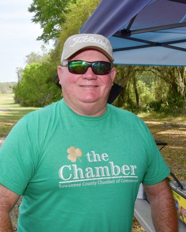 Man in green shirt and sunglasses, wearing a Titleist hat, smiling outdoors near a tent.