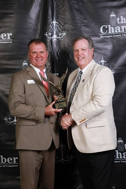 Two men in suits holding an award at an event with a dark backdrop.
