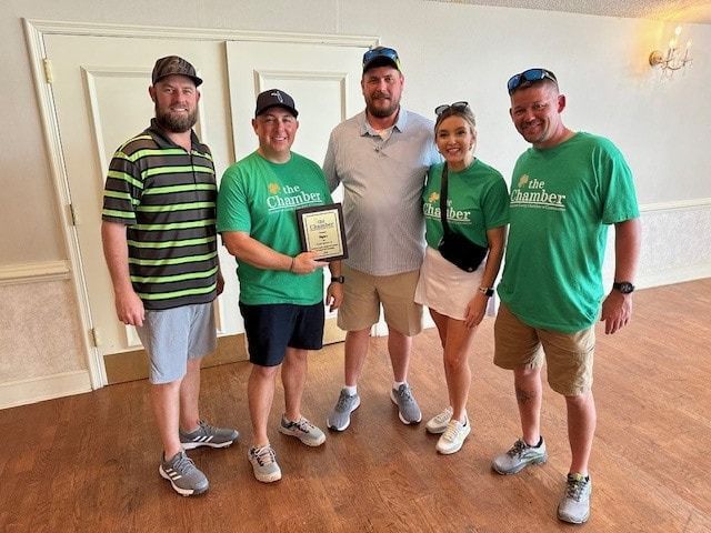 Five people in green shirts holding an award, smiling indoors.
