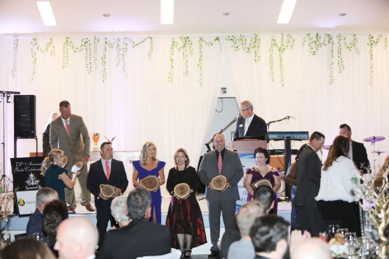 People on stage holding awards at an event, with a speaker and band in the background.
