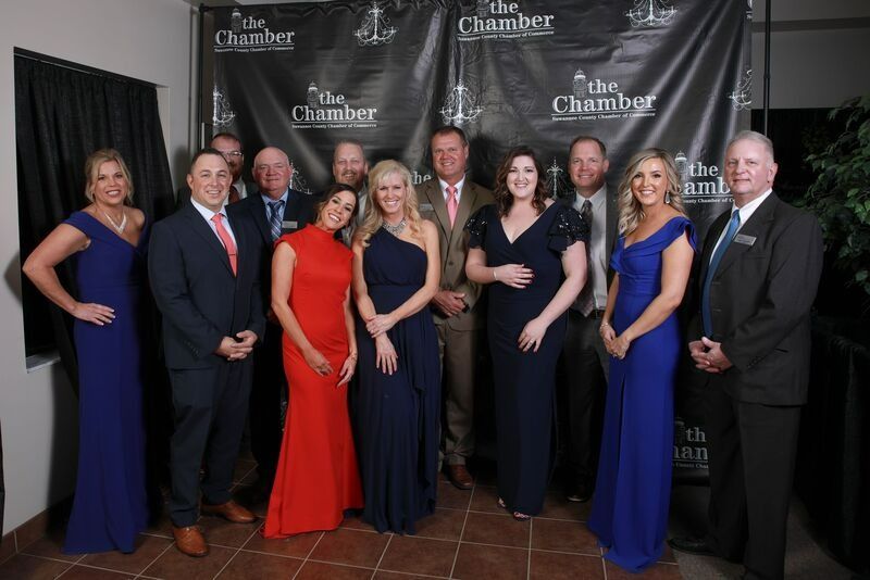 Group of formally dressed people posing in front of a banner at an event.