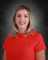 Woman in red dress smiles, headshot. Dark background.