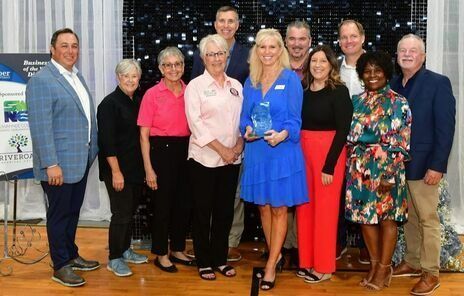 Group of people smiling, holding a blue award. Indoor setting with a backdrop, logo, and a blue and white theme.