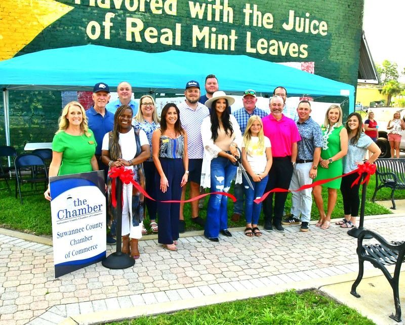 People cutting a ribbon in front of a building with a mural. A sign for the Chamber of Commerce is in front.