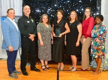 Group of people holding an award, smiling, standing in front of a sparkly backdrop.