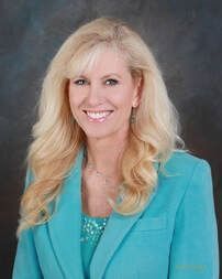 Woman with blonde hair, wearing a turquoise blazer and smiling.