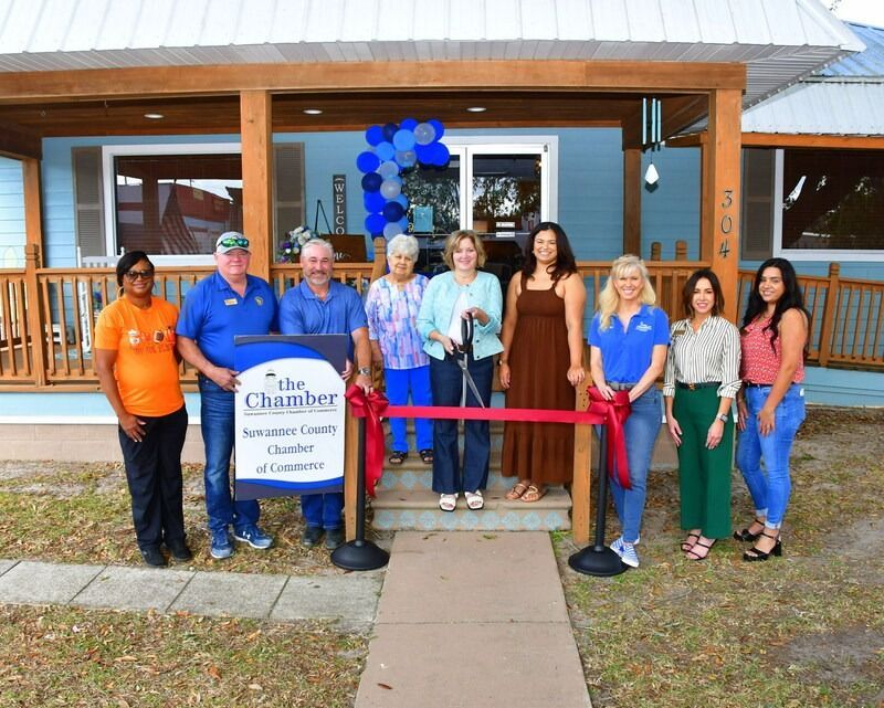 Group of people at a ribbon-cutting ceremony in front of a blue building with a Chamber sign.