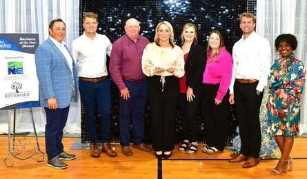Group of people posing for a photo at an event, standing in front of a backdrop with a sign.