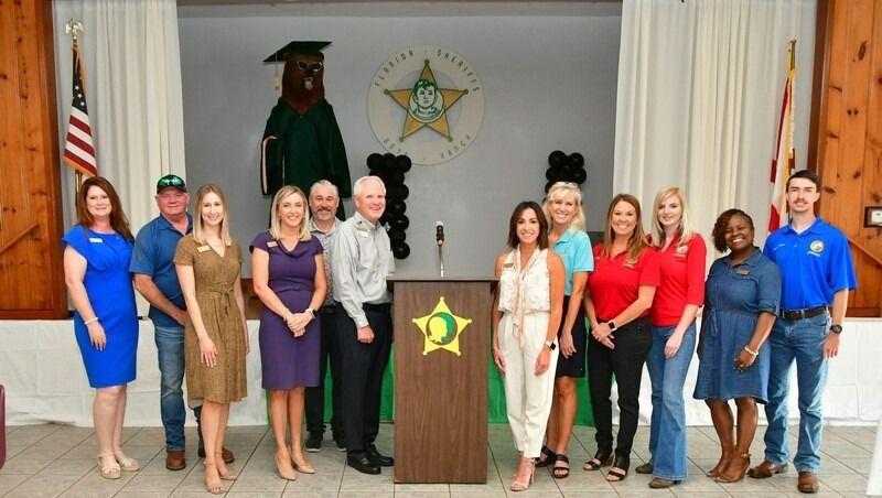 Group of people standing behind a podium with a sheriff's star and bear statue in the background.