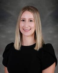 Woman with blonde hair smiling, wearing a black top, against a gray background.