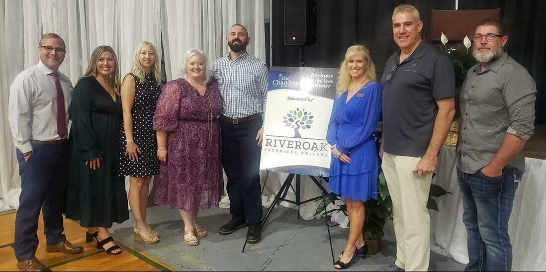 Group of people standing in front of a sign with a tree logo.