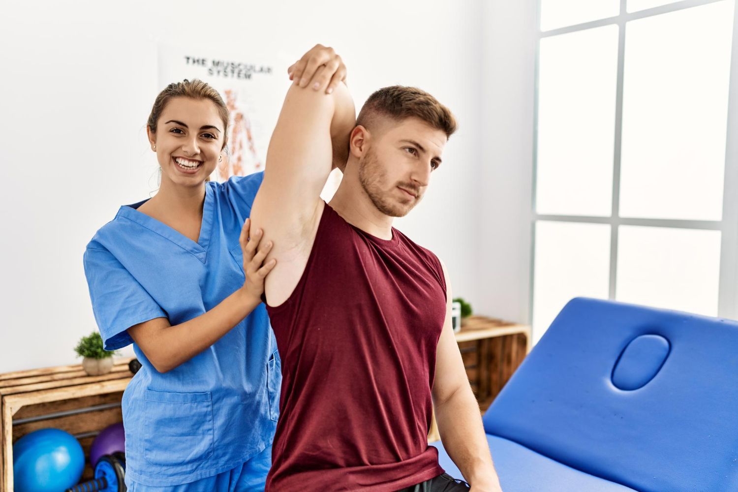 A woman is helping a man stretch his arm in a hospital.